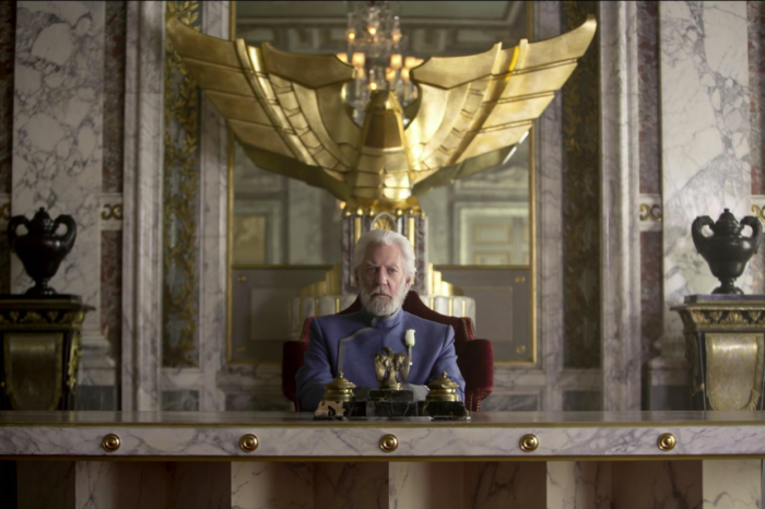 President Snow from the Hunger Games film sitting in a gold and white marble office.